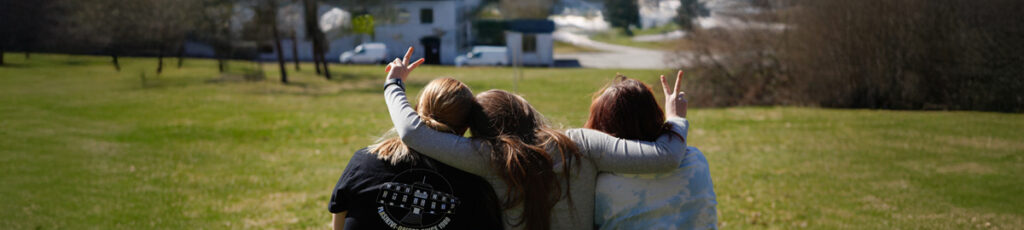 Kolme media-alan koulutuksen opiskelijaa istuvat ruohikolla. 